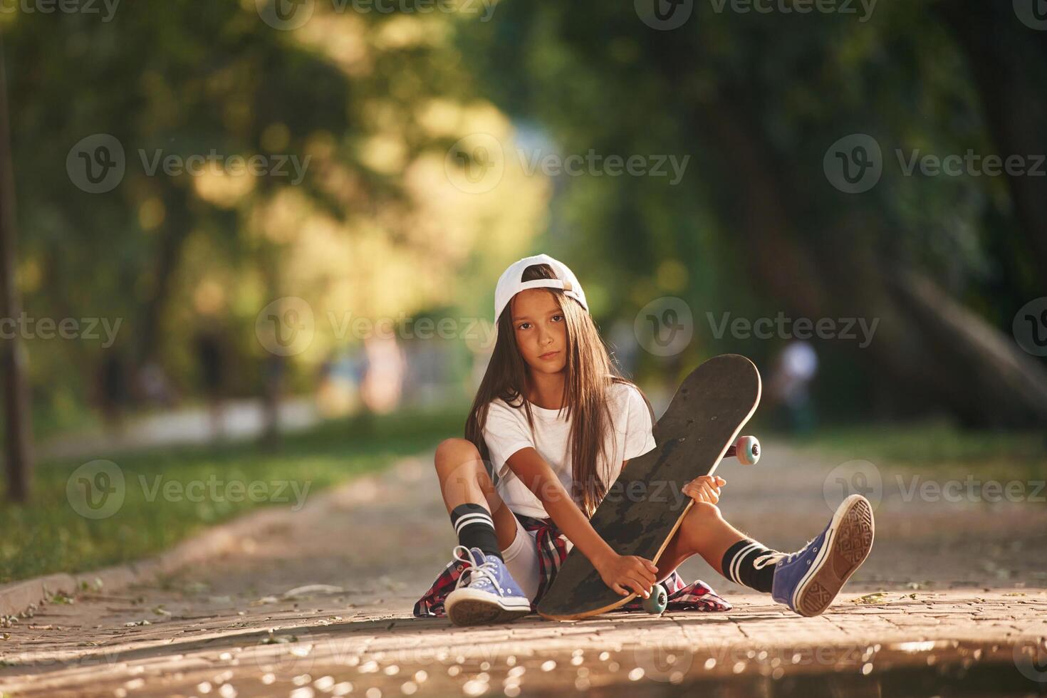 Green ,trees are, in the background, on the path. Happy little girl with skateboard outdoors photo