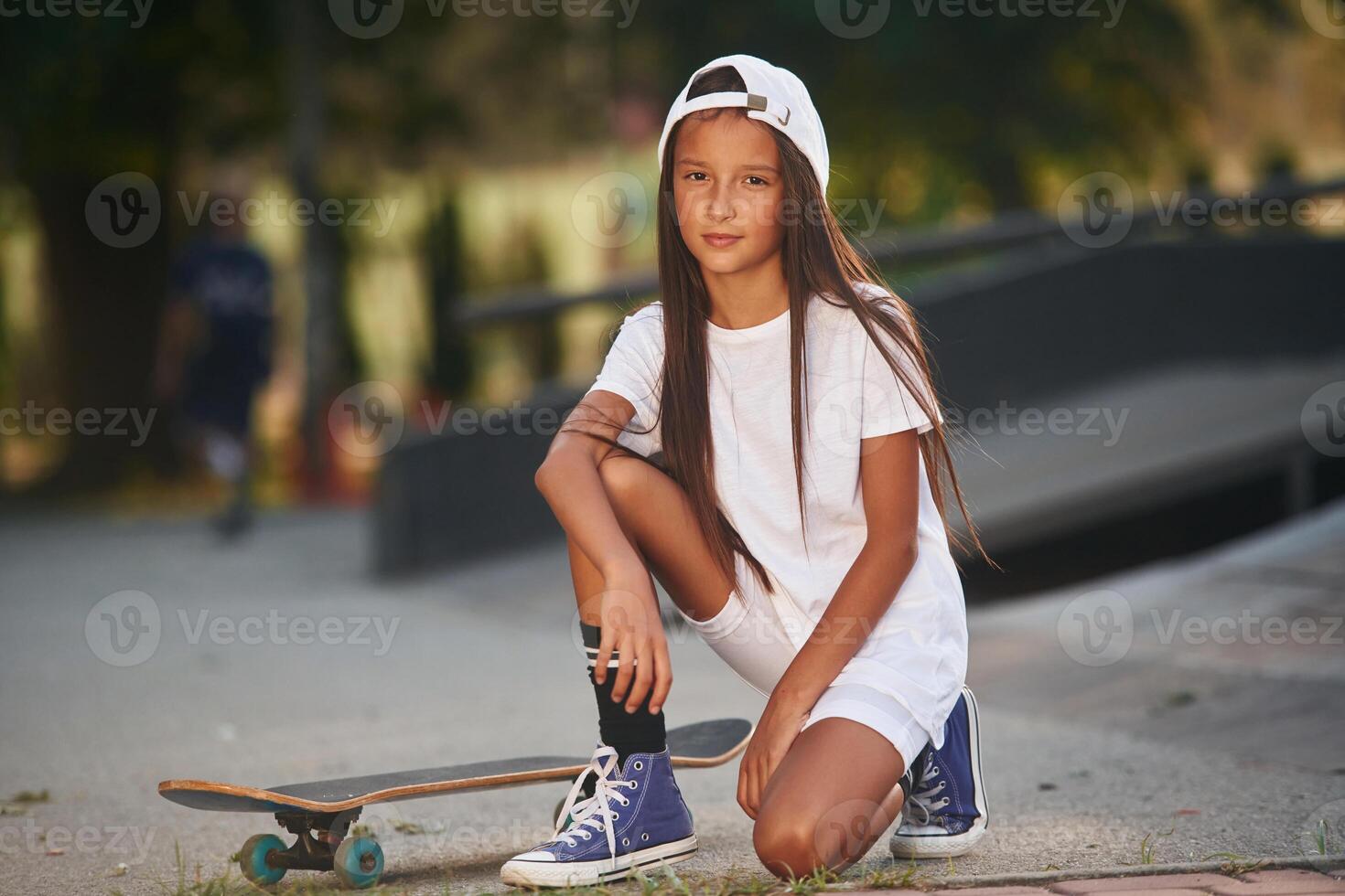 Ramp is behind. Girl, is ,sitting. With skateboard outdoors photo