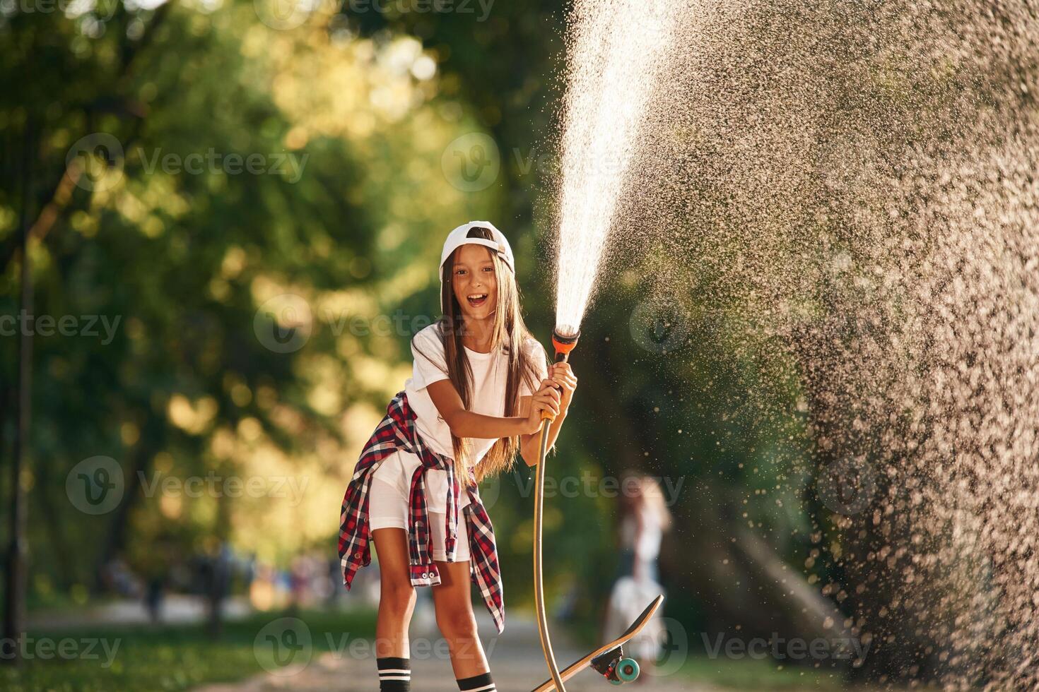 Plays, with, water as it pours from a hose. Happy little girl with skateboard outdoors photo