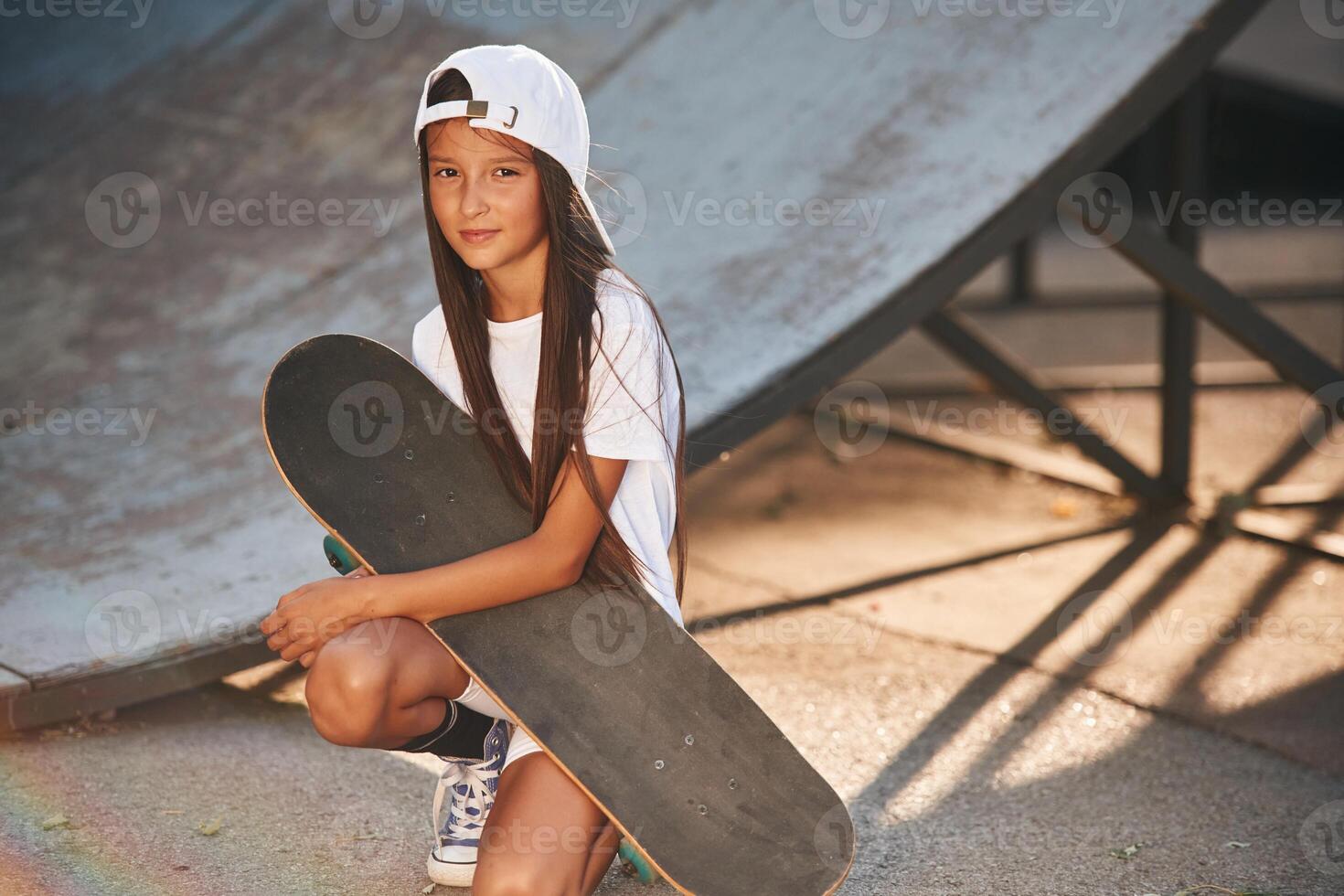 Ramp, is behind. Girl is sitting. With skateboard outdoors photo