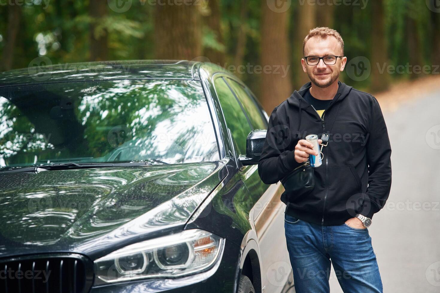 Man, in jeans is near his modern black car outdoors photo