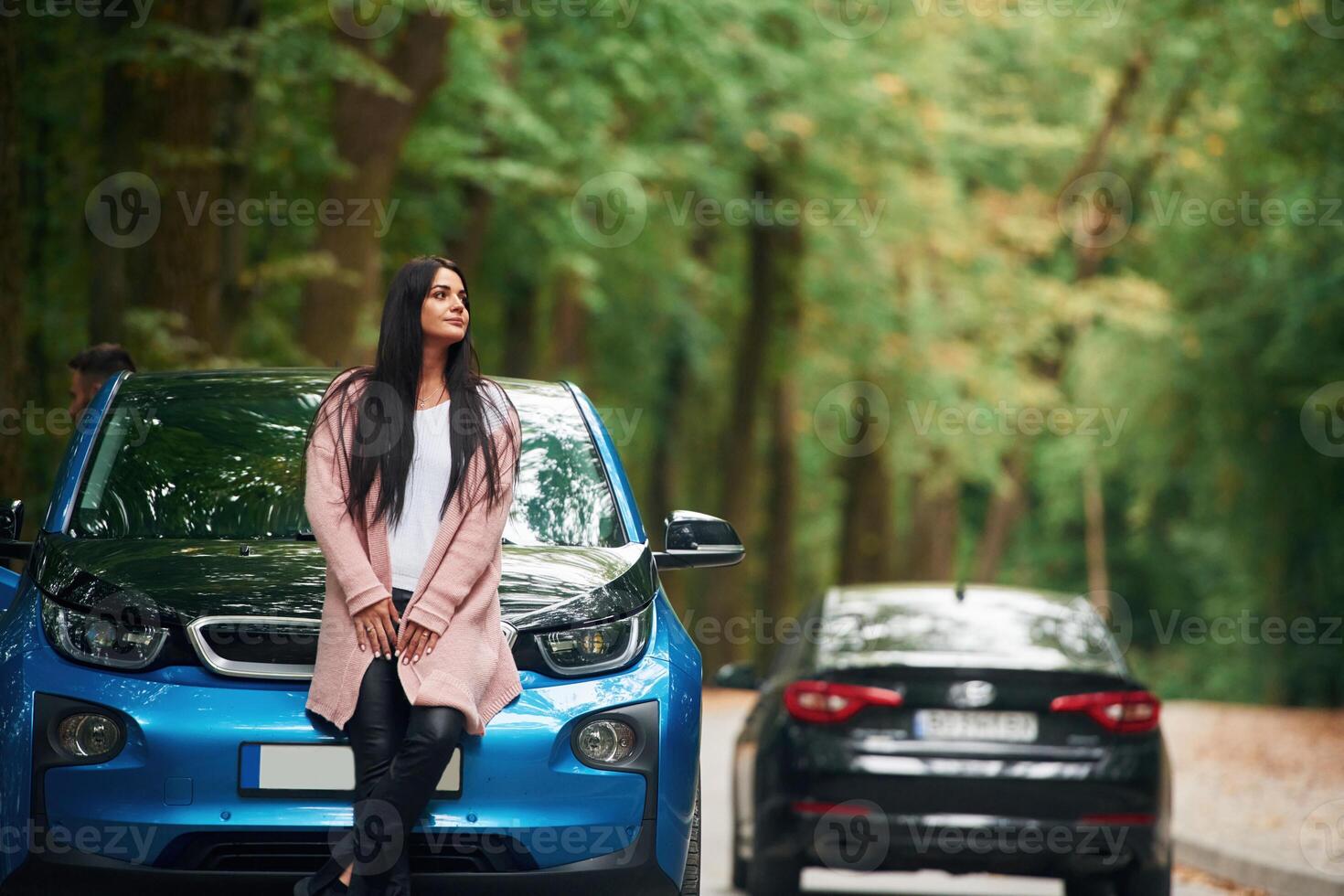 Black automobile, behind. Cheerful ,beautiful woman is near blue car outdoors photo