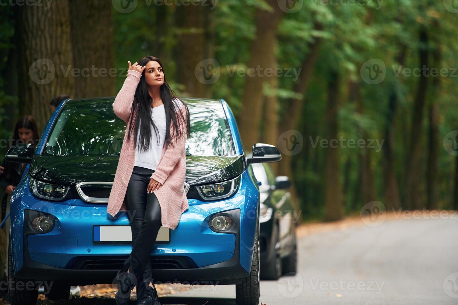 Black, automobile ,behind. Cheerful beautiful woman is near blue car outdoors photo