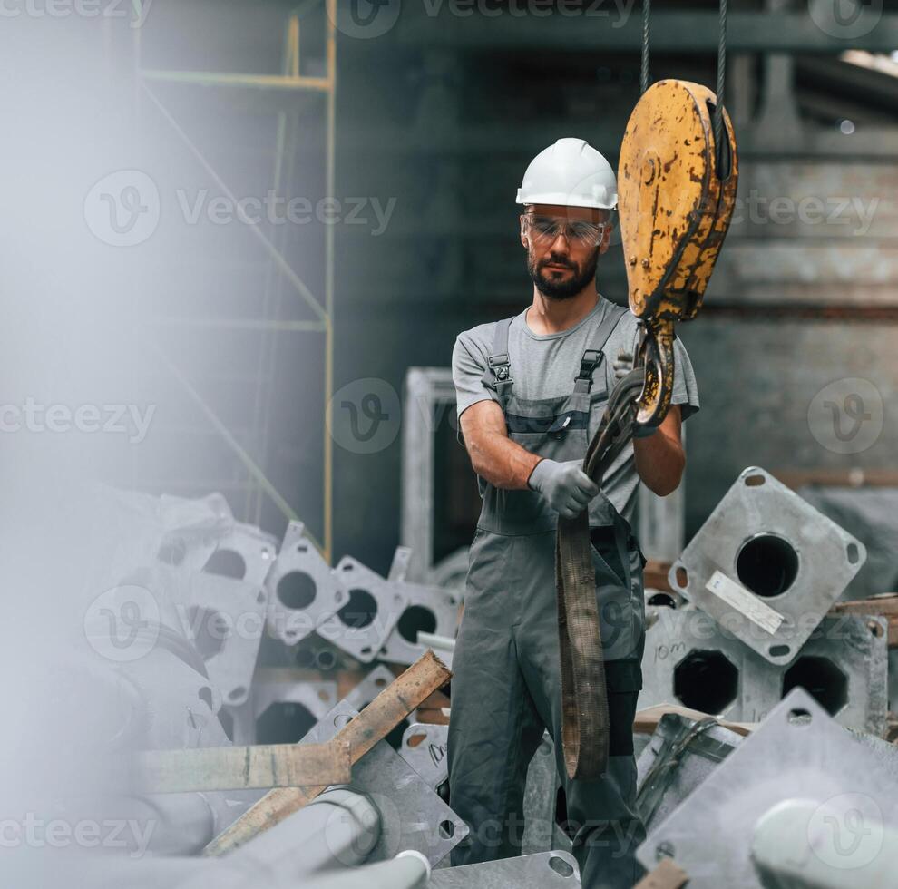 Using crane hook. Young factory worker in grey uniform photo