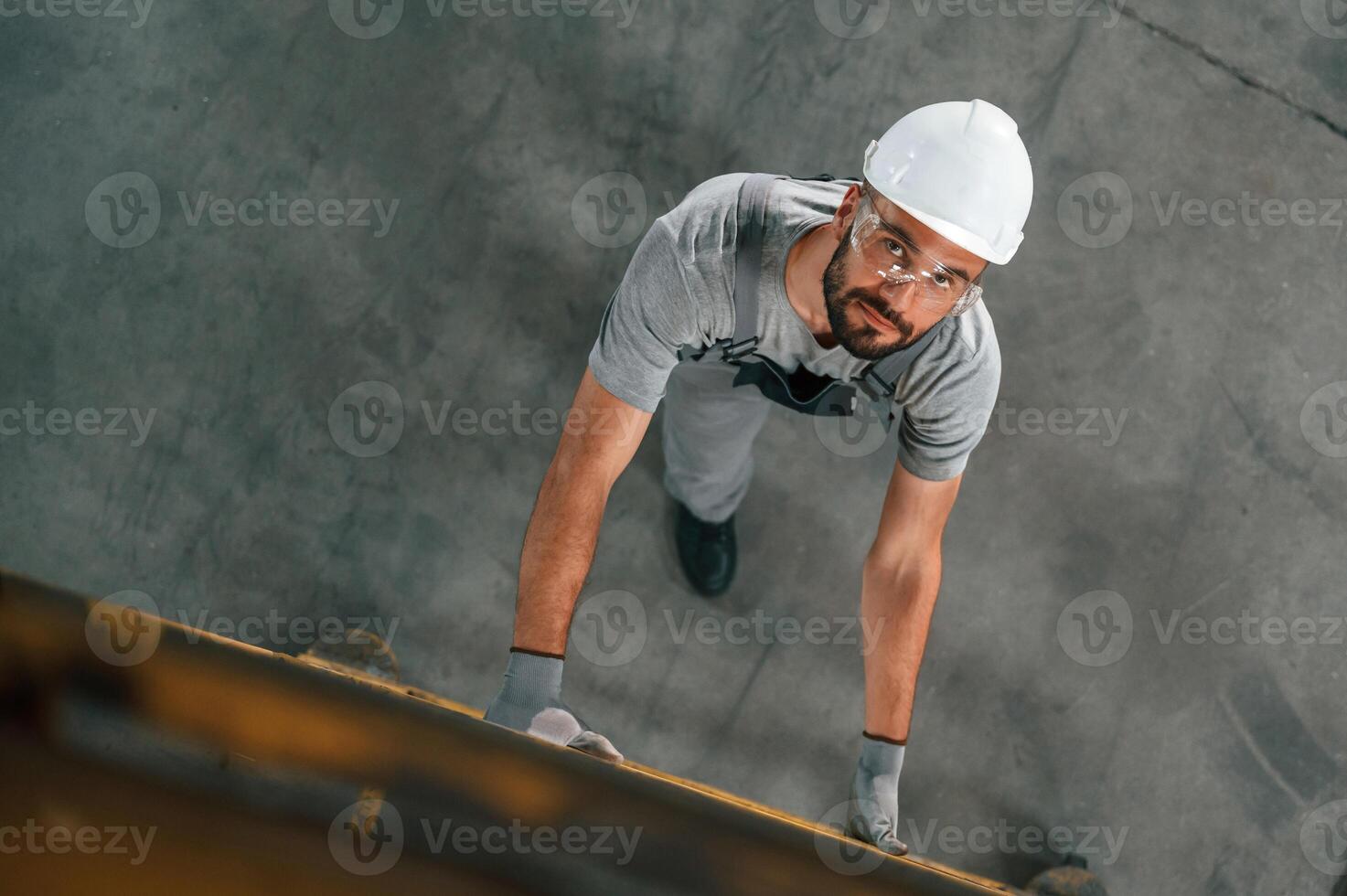 Going up, on the, ladder, top view. Young factory worker in grey uniform photo