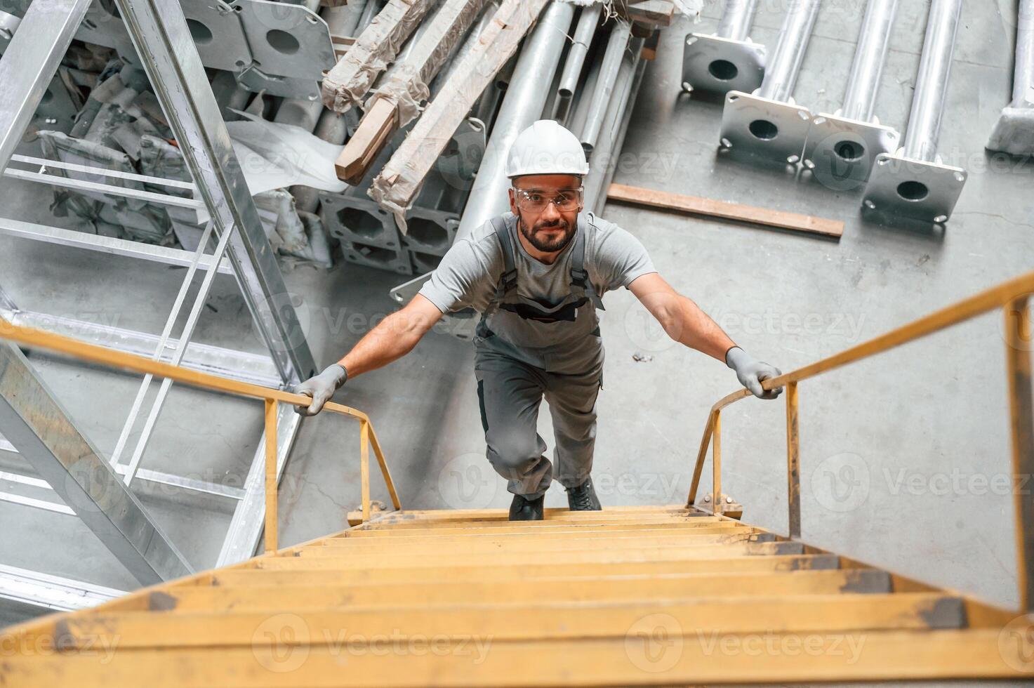 Climbing up, on ,the ladder. Young factory worker in grey uniform photo