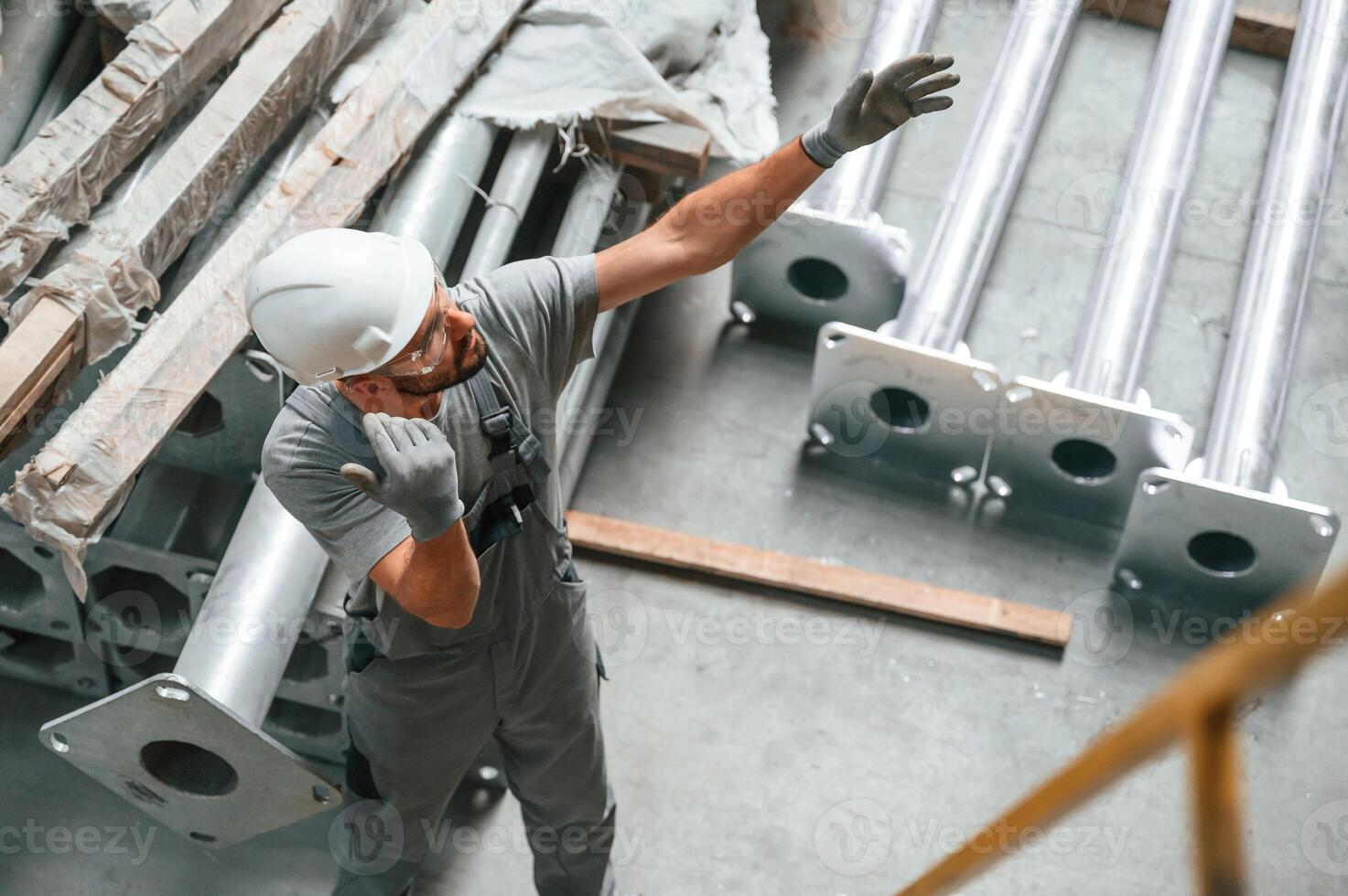 Top view. Making gesture, by ,hands. Young factory worker in grey uniform photo
