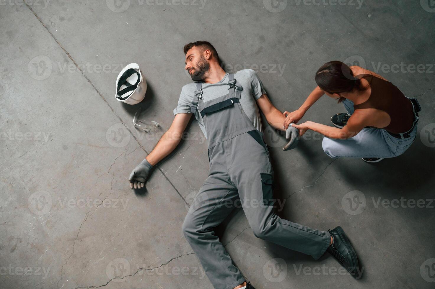 Woman hands checking pulse.. Accident, male factory worker fell, without consciousness, lying down on the floor photo