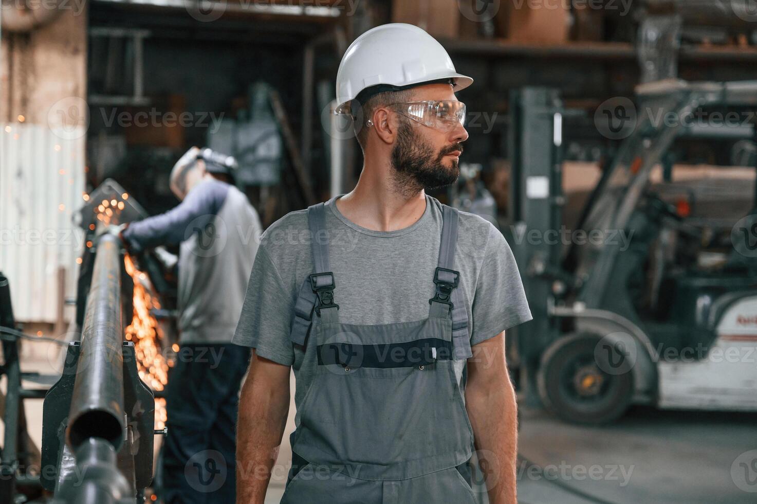 Another ,man is behind. Young factory worker in grey uniform photo