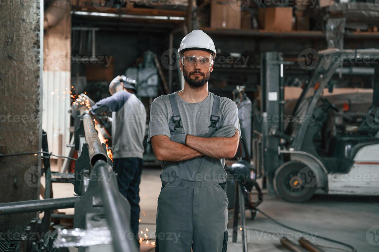 Another man, is behind. Young factory worker in grey uniform photo