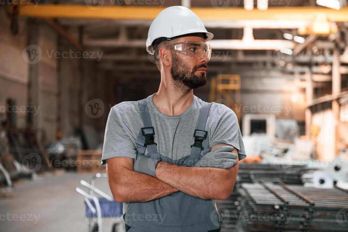 Standing with arms crossed.. Young factory worker in grey uniform photo