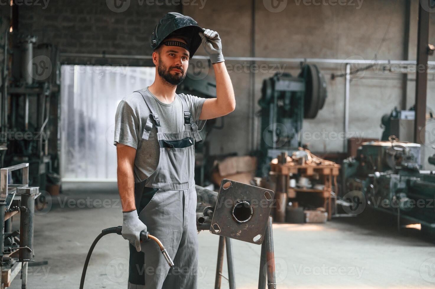Taking ,a break. With welding equipment. Young factory worker in grey uniform photo