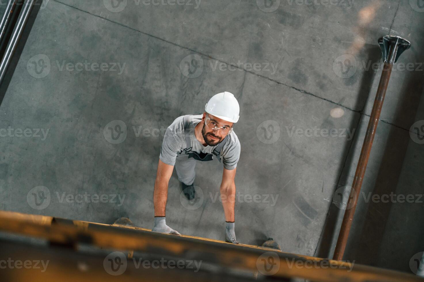 Going, up, on the ladder, top view. Young factory worker in grey uniform photo