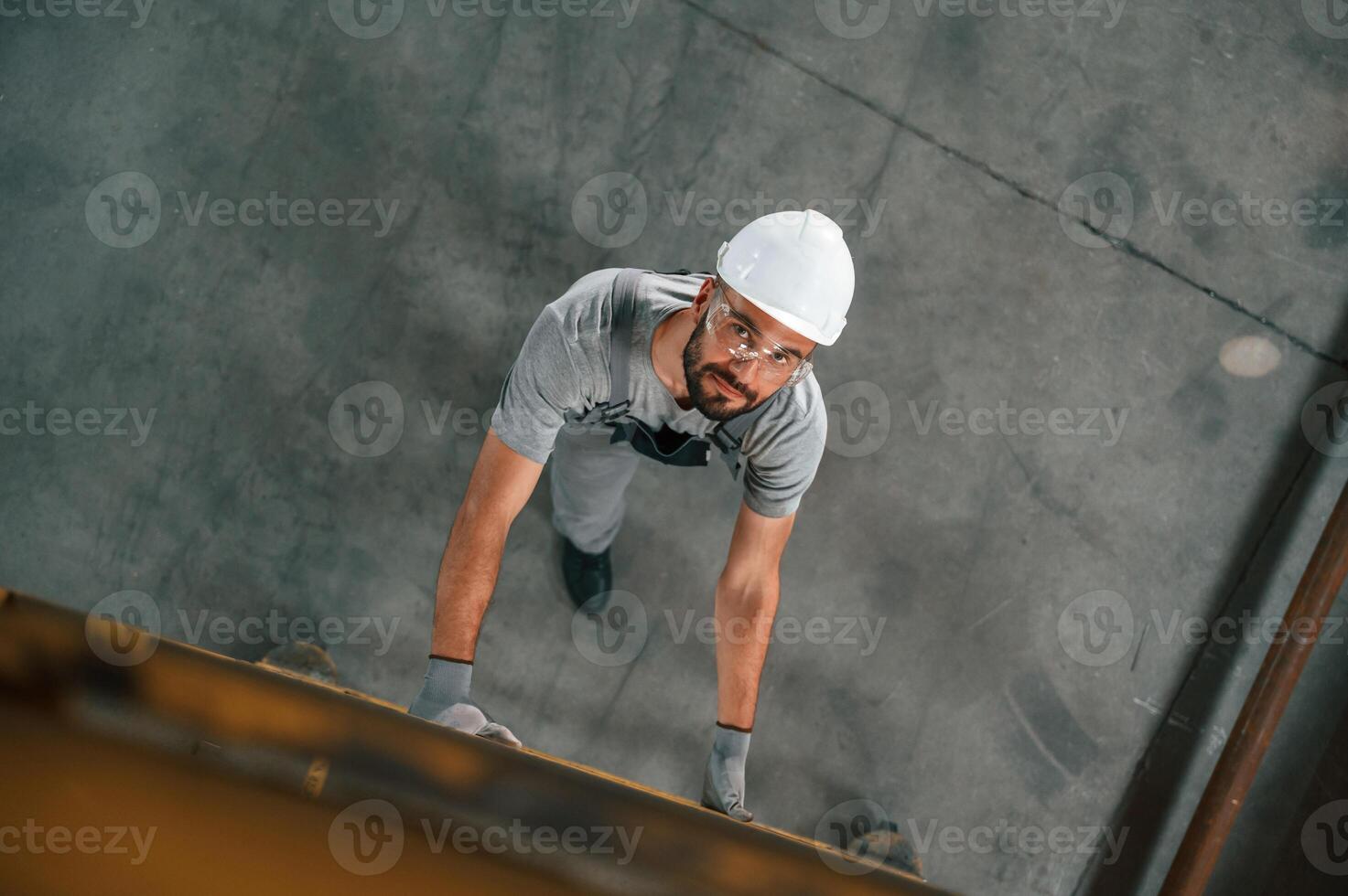 Going up, on the ladder, top view. Young factory worker in grey uniform photo