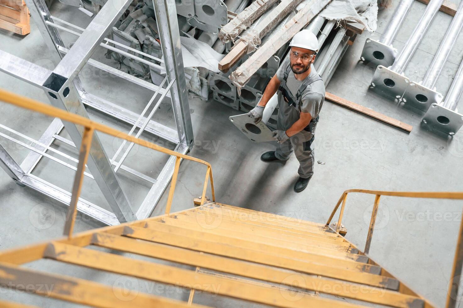 Climbing, up on the ladder. Young factory worker in grey uniform photo