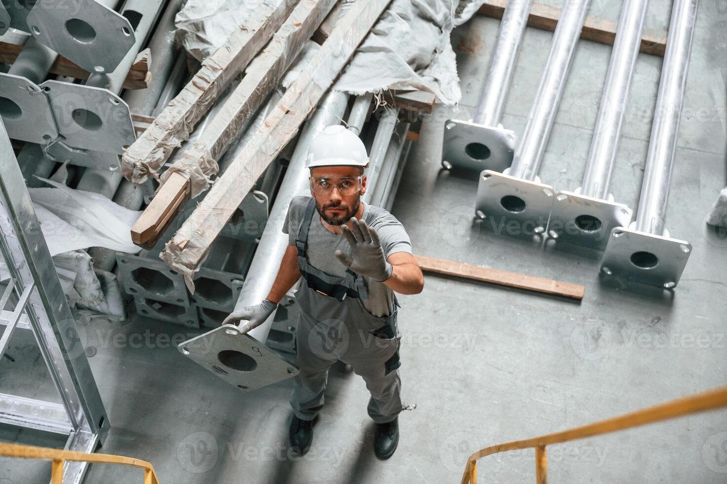 Top, view. Making gesture by hands. Young factory worker in grey uniform photo