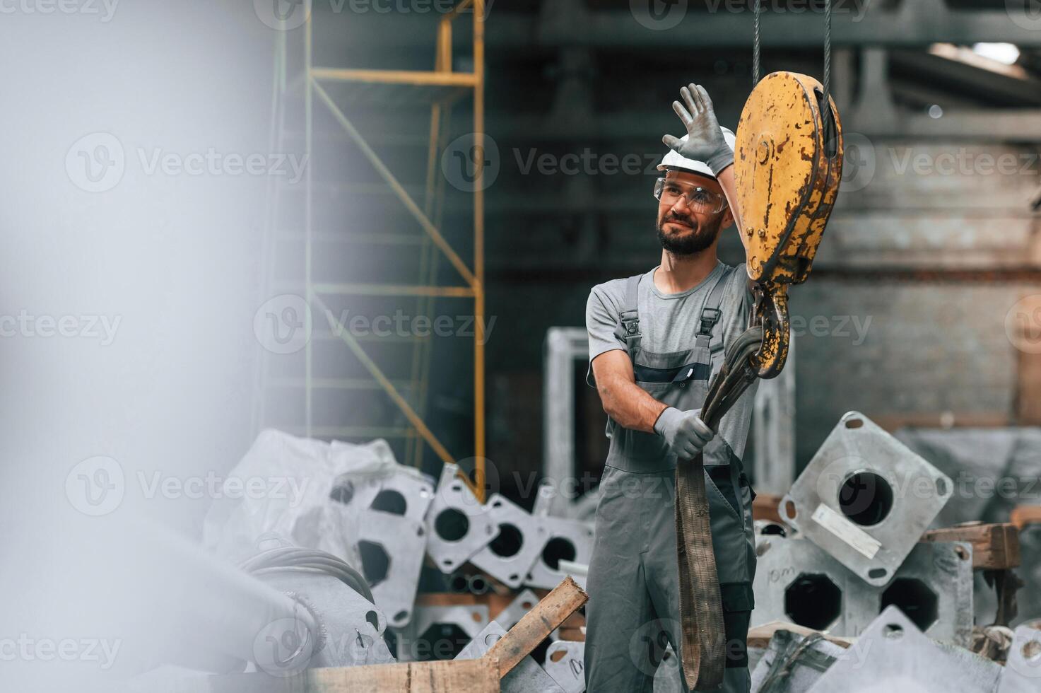 Using ,crane ,hook.. Young factory worker in grey uniform photo