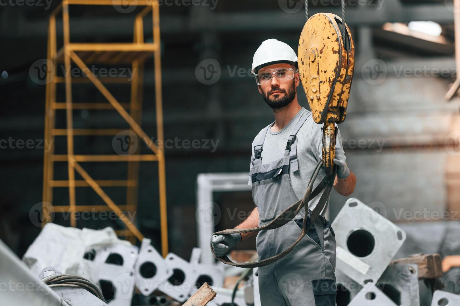 Using ,crane hook.. Young factory worker in grey uniform photo