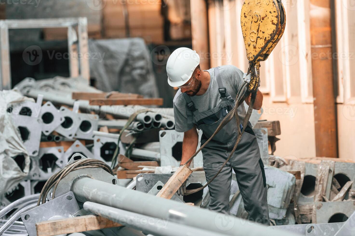 Using, crane hook. Young factory worker in grey uniform photo