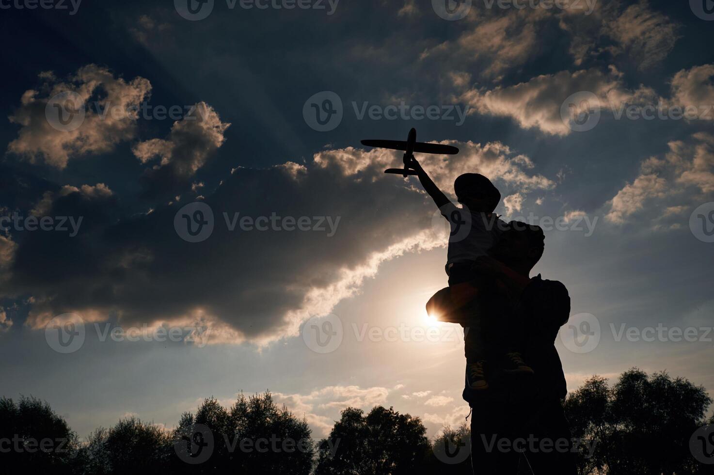 Against ,dramatic sky, with, toy, plane, sitting on shoulders. Father and little son are playing and having fun outdoors photo