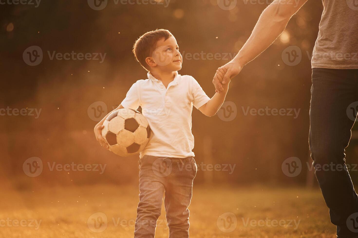 Illuminated by sunlight, holding soccer ball. Father and little son are playing and having fun outdoors photo