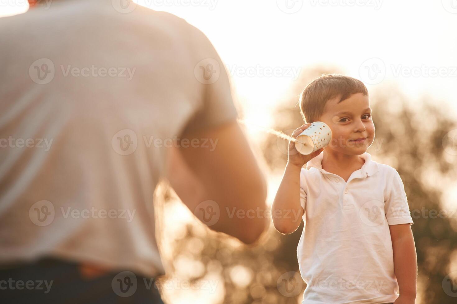 Fun,,, holding and using string can phone. Father and little son are playing outdoors photo