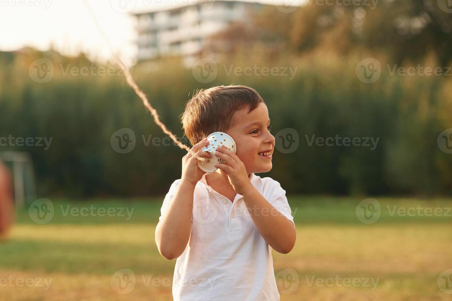 Using string can phone. Little boy is playing outdoors at daytime photo
