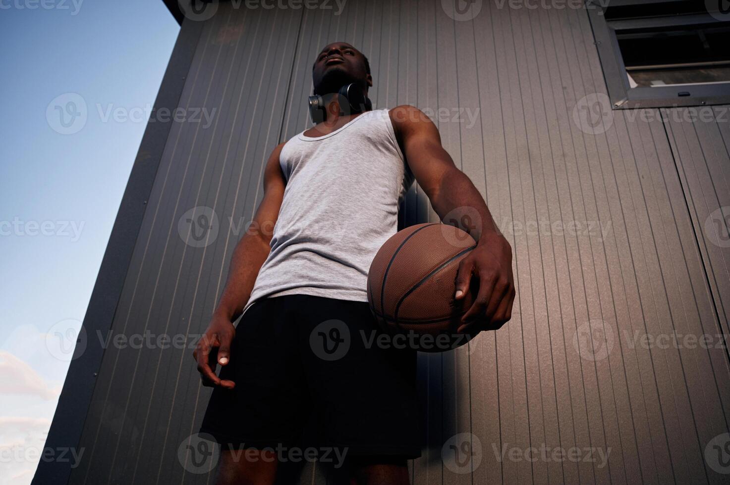 Standing,, against metal surface building. Young black man is with basketball ball outdoors photo
