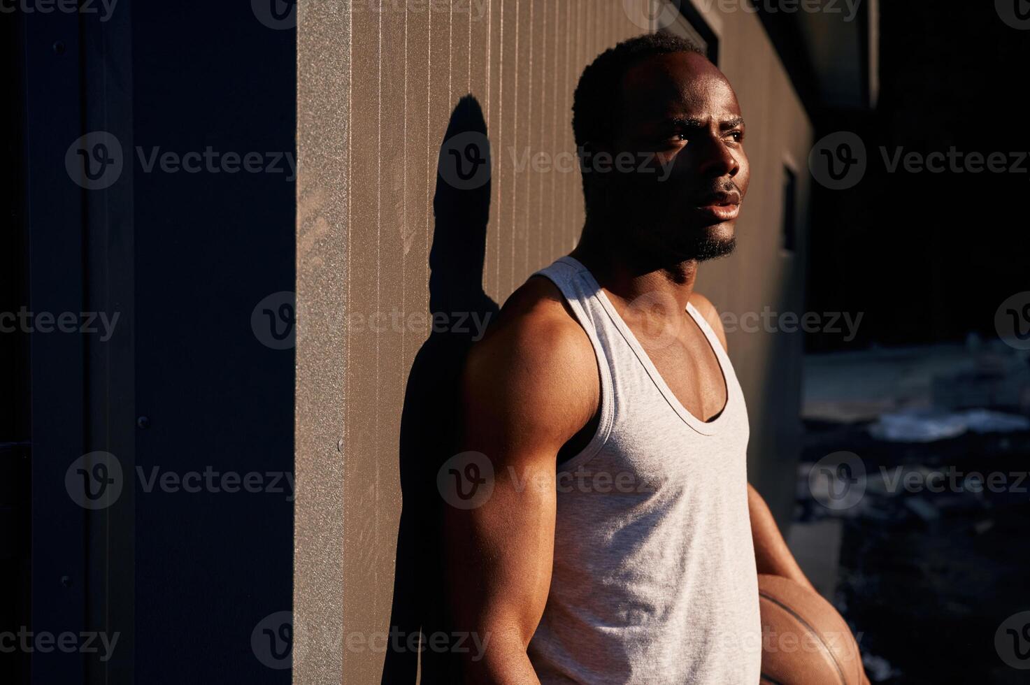 Standing, against metal surface, building. Young black man is with basketball ball outdoors photo