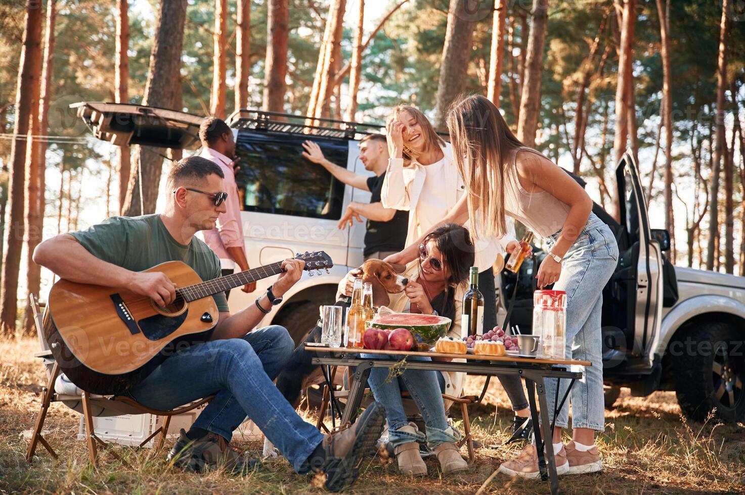 Man, is, playing guitar, by table. Group of friends are together in the forest photo