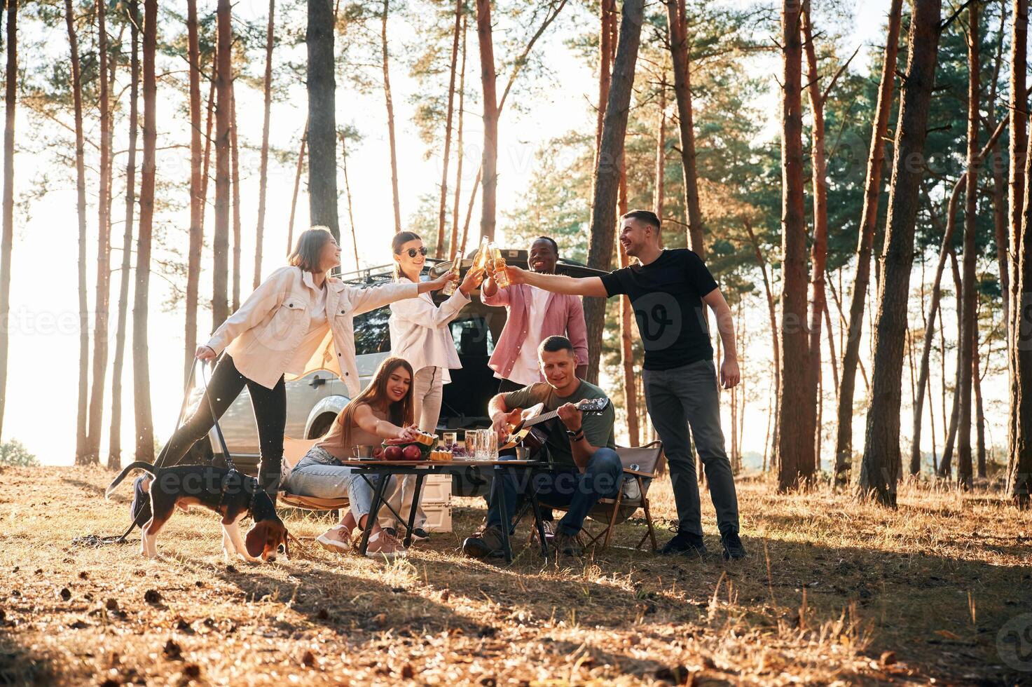 Doing cheers ,with ,bottles of beer. Group of friends are together in the forest photo