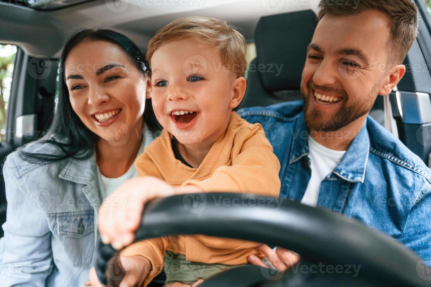 Boy, is trying to ride. Family of father, mother and little son are sitting in the modern car photo
