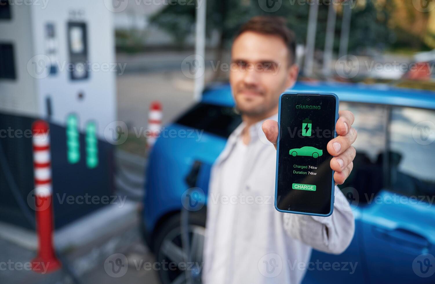 Charging process on the display of smartphone. Man with blue electric car on the station photo