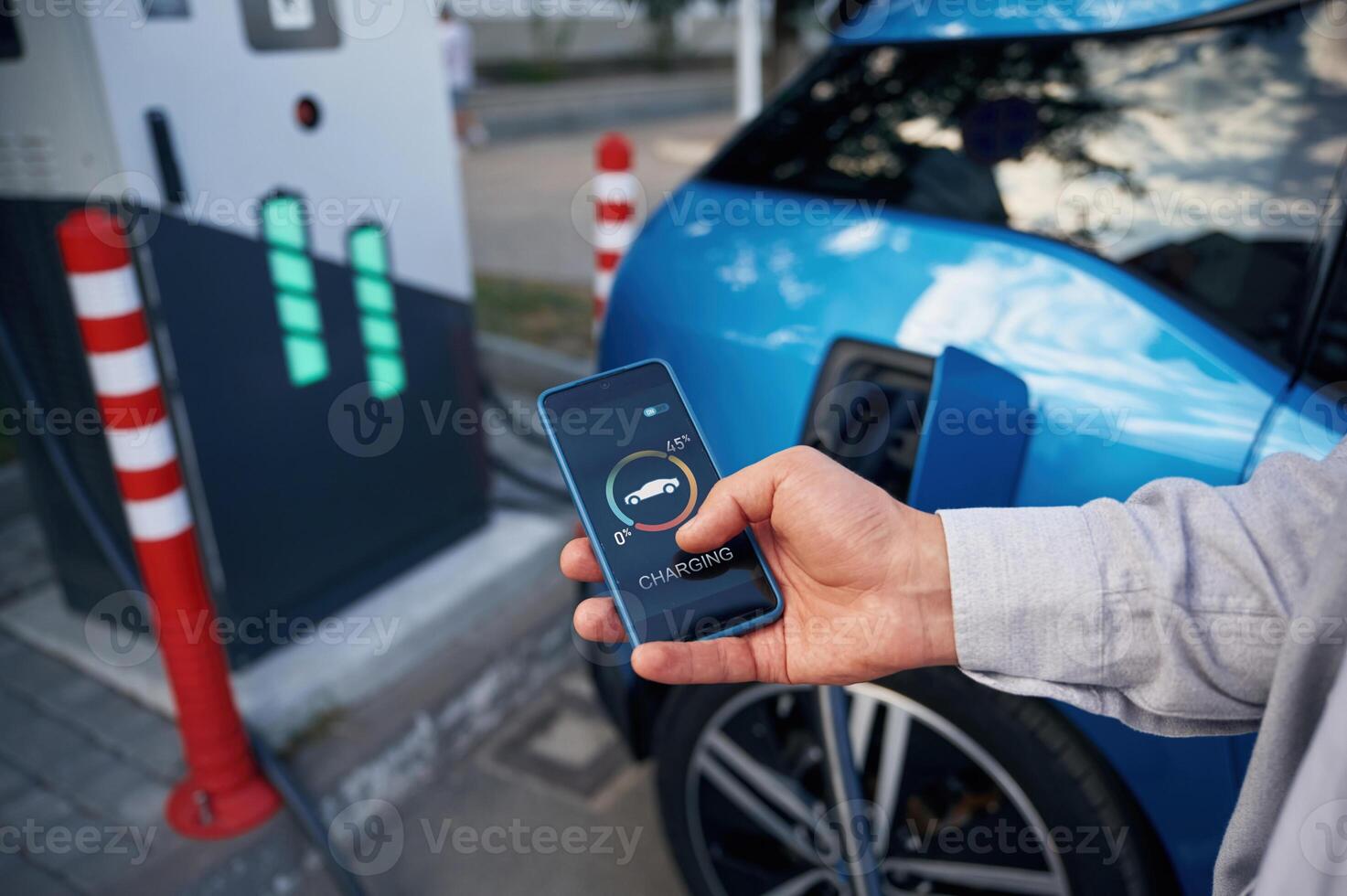 Showing process on the display of smartphone. Man with blue electric car on the charge ,,station photo