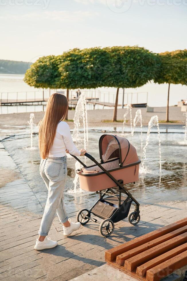 Young woman is with pram, walking, outdoors photo