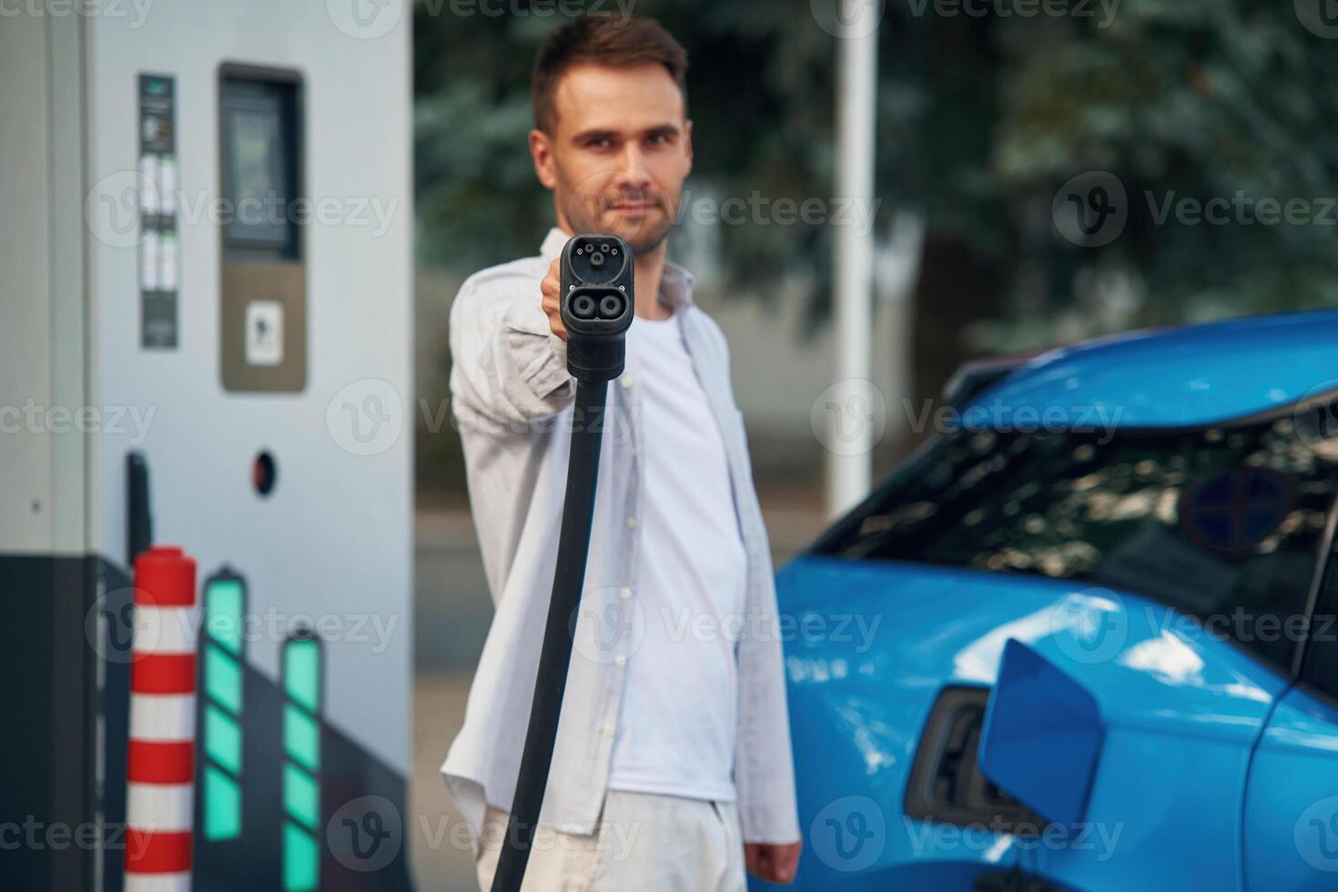 Holding wire, in hand. Man with blue electric car on the charge station photo