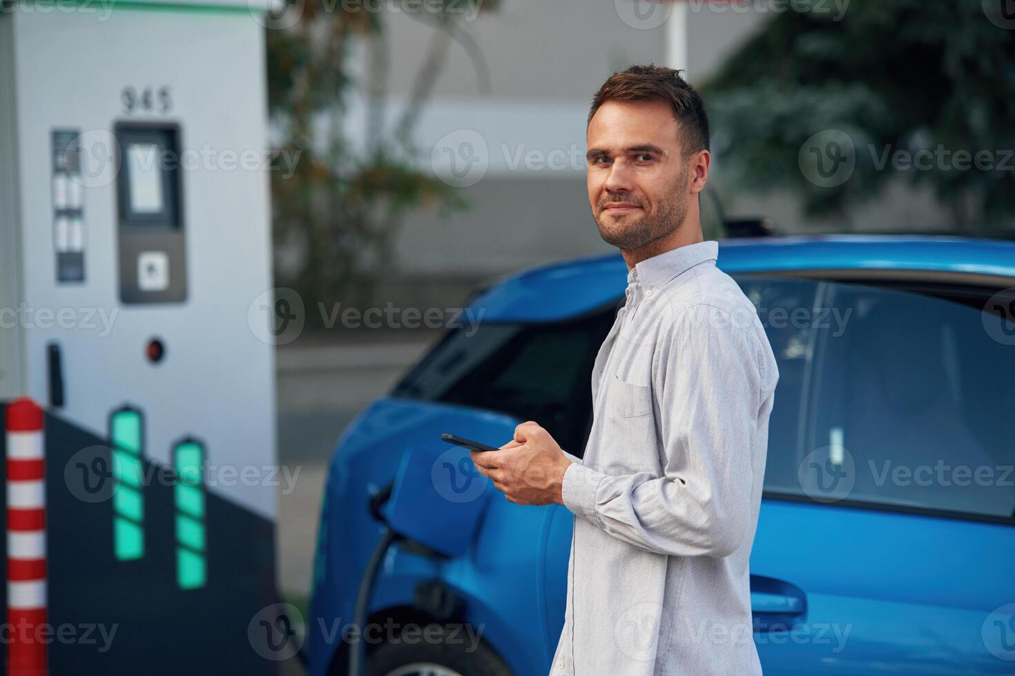 Blue, vehicle, holding ,smartphone. Man with blue electric car on the charge station photo
