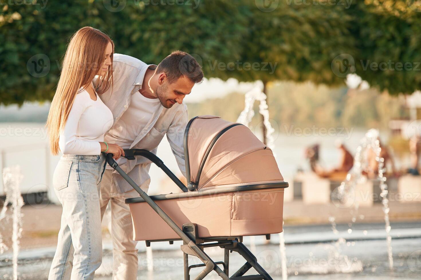 A young couple with a baby, pram, is walking together photo