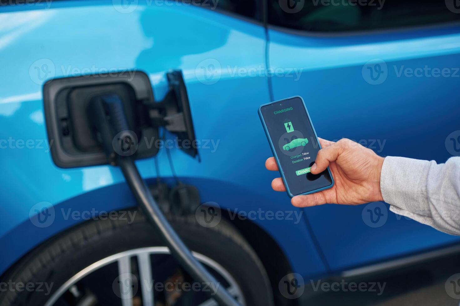 Charging process on, the ,display of smartphone. Man with blue electric car on the station photo