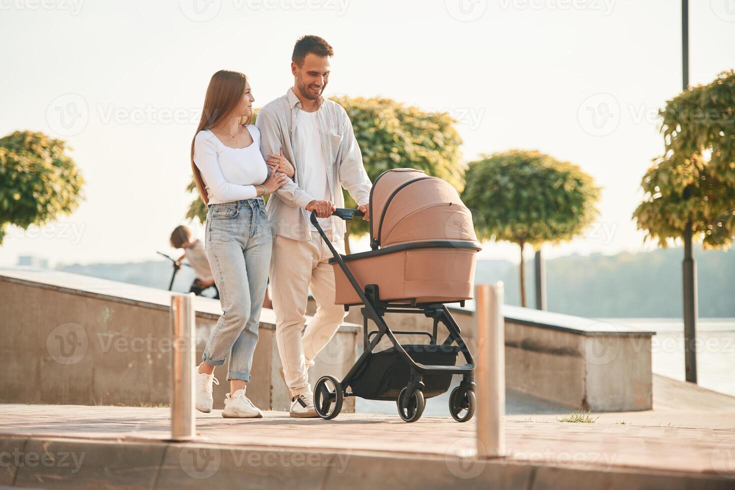 Little, green trees behind.. A young couple with a baby pram is walking together photo