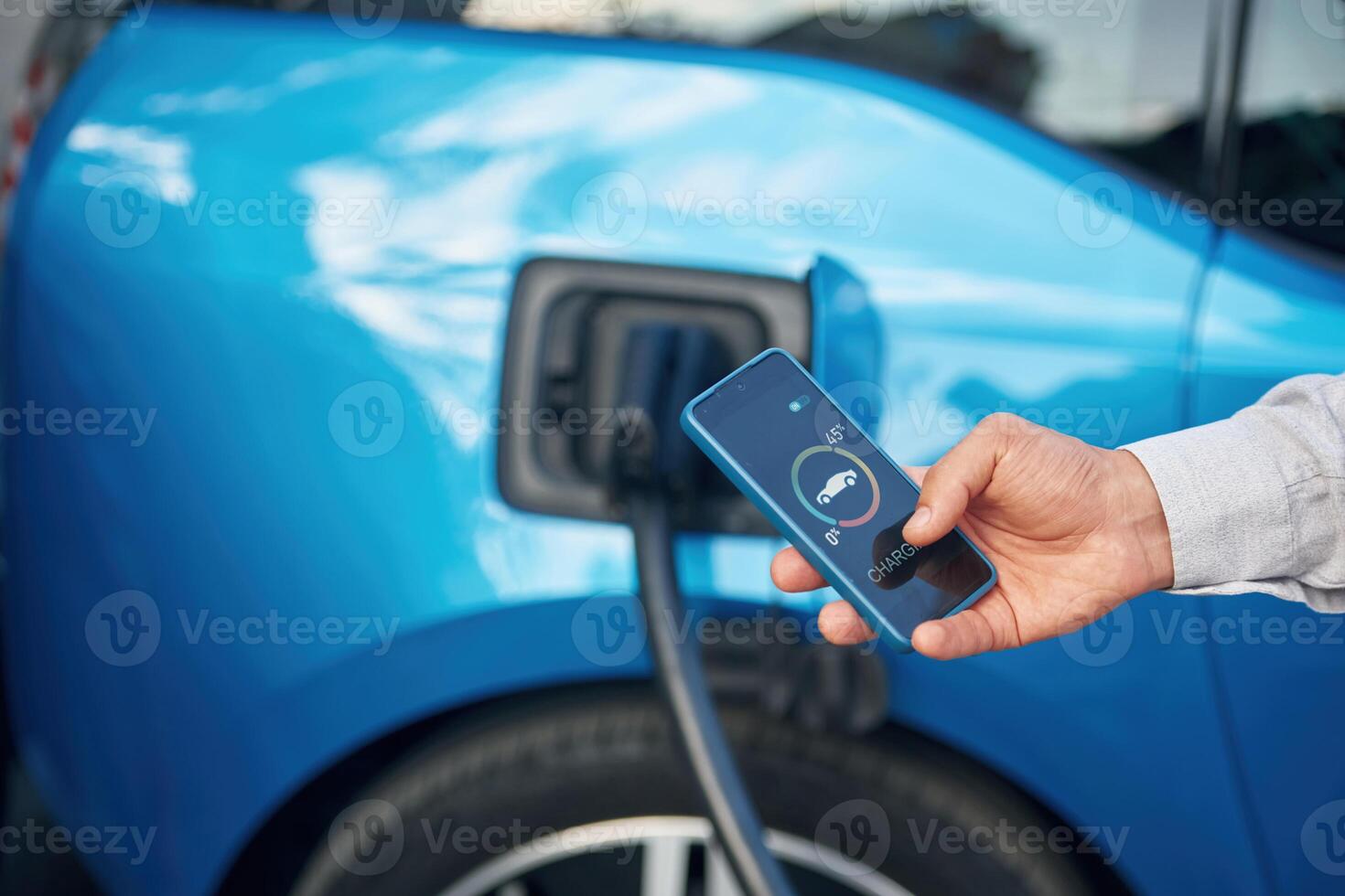 Charging process,, on the display of smartphone. Man with blue electric car on the station photo