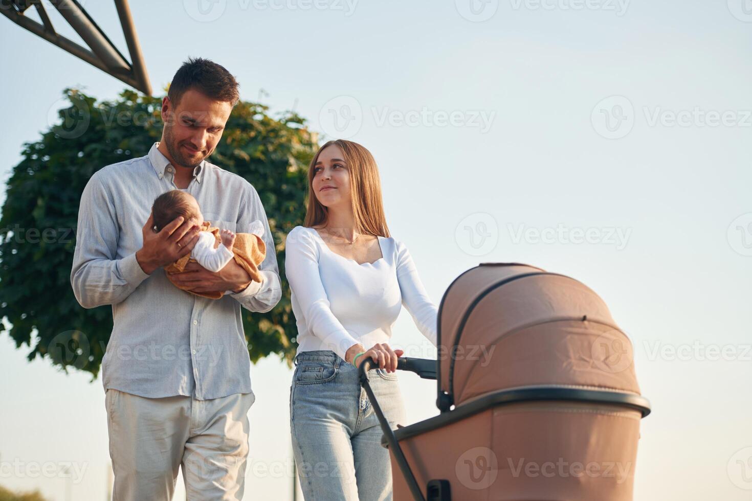 Holding, baby in hands. A young couple with a pram is walking together photo