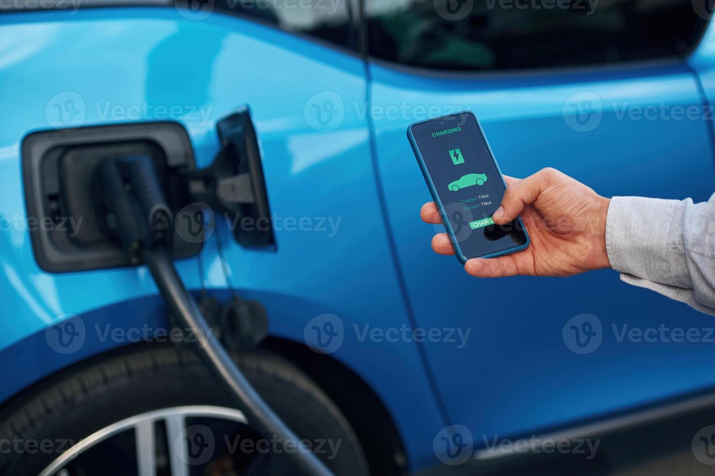 Charging, process on the display of smartphone. Man with blue electric car on the station photo