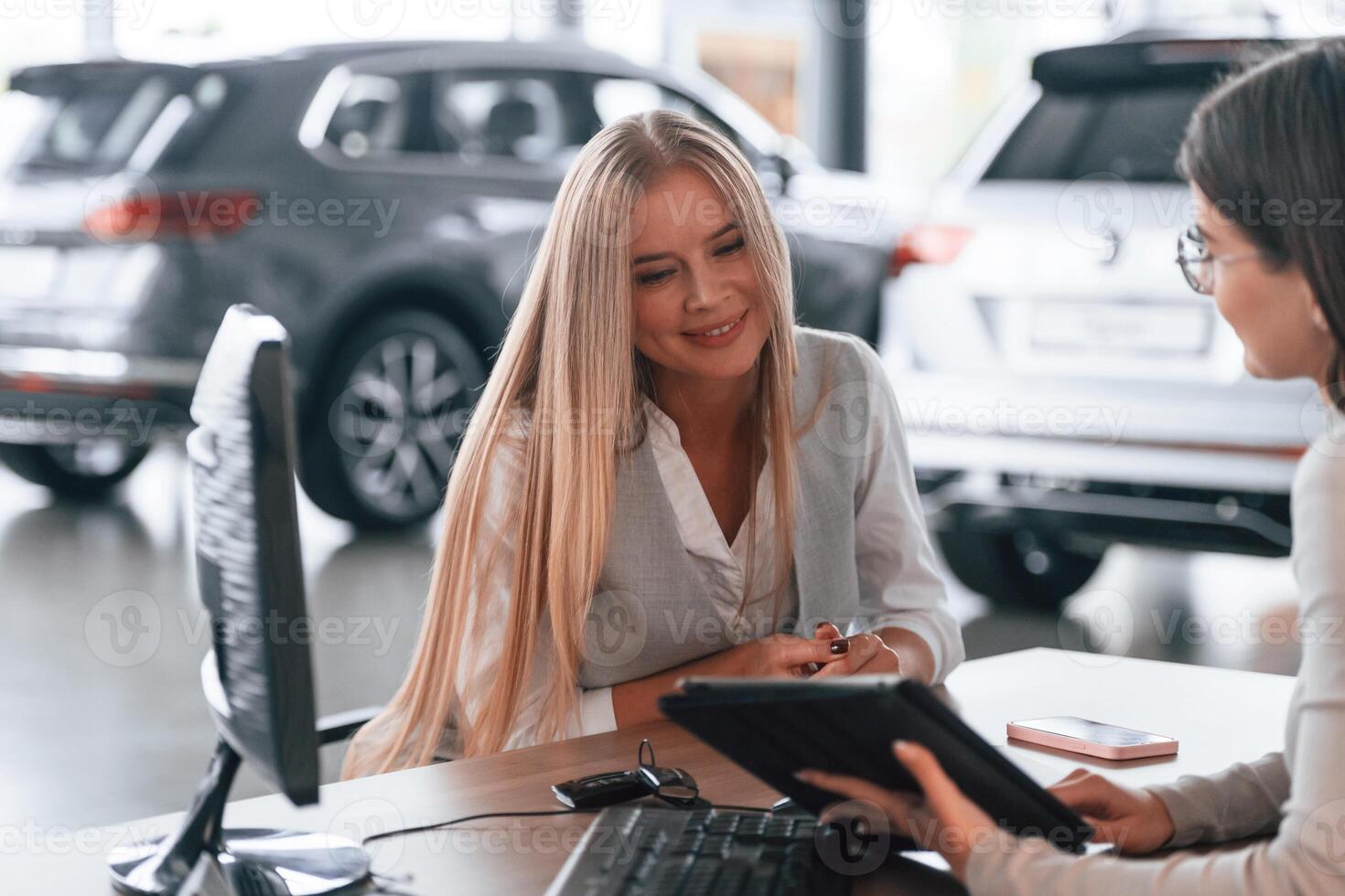 Sitting by the ,table. Female manager is helping woman customer in the car dealership salon photo