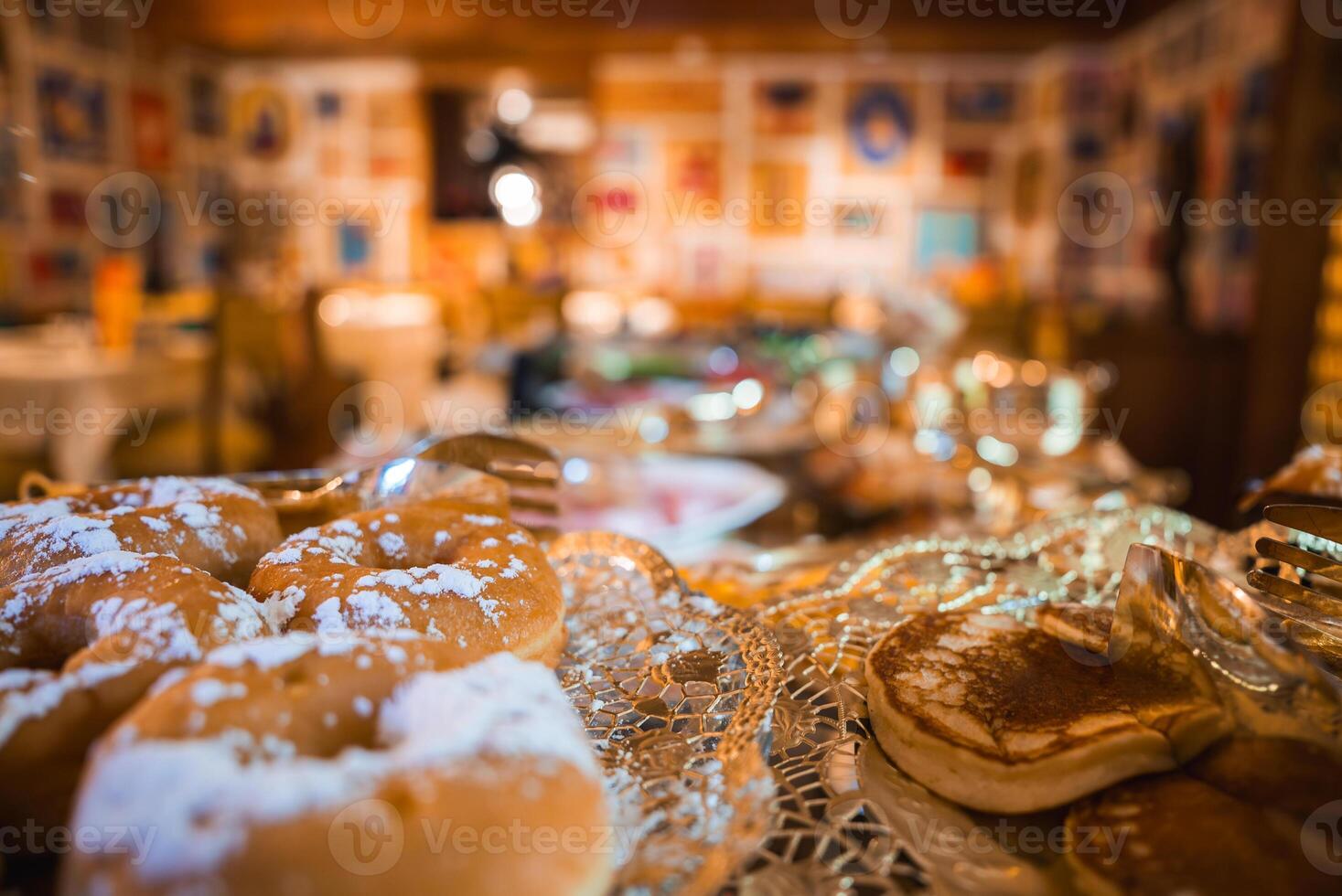 Close up of pastries and pancakes on a lace patterned tray in a rustic dining area with wooden walls, framed artwork, and soft lighting in Cortina, Italy. photo