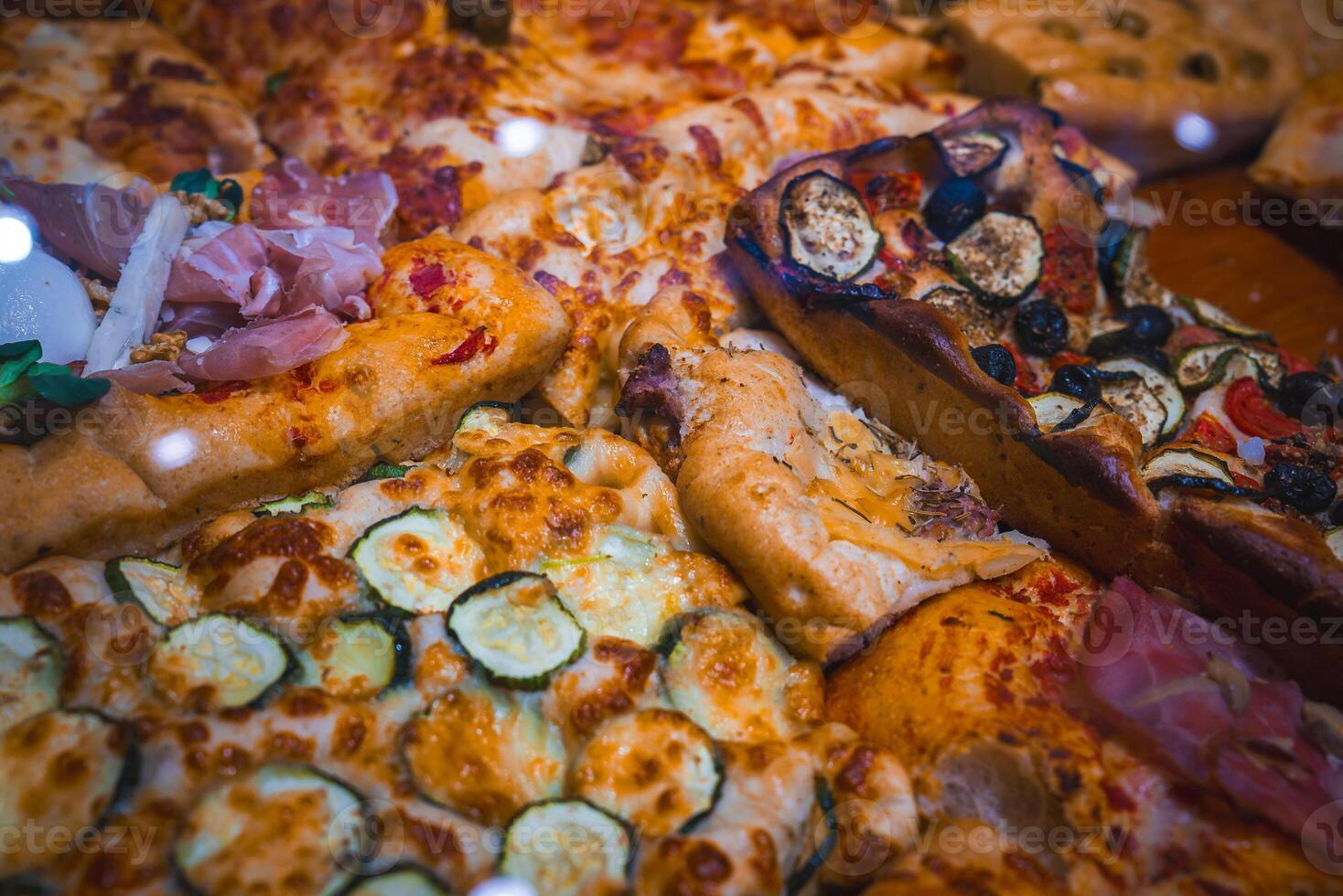 A close up view of freshly baked Italian pizzas in Bergamo, Italy, featuring toppings like zucchini, prosciutto, mozzarella, eggplant, olives, and tomatoes. photo