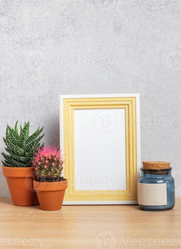 Empty photo frame with cacti, candle and copy space on wooden table