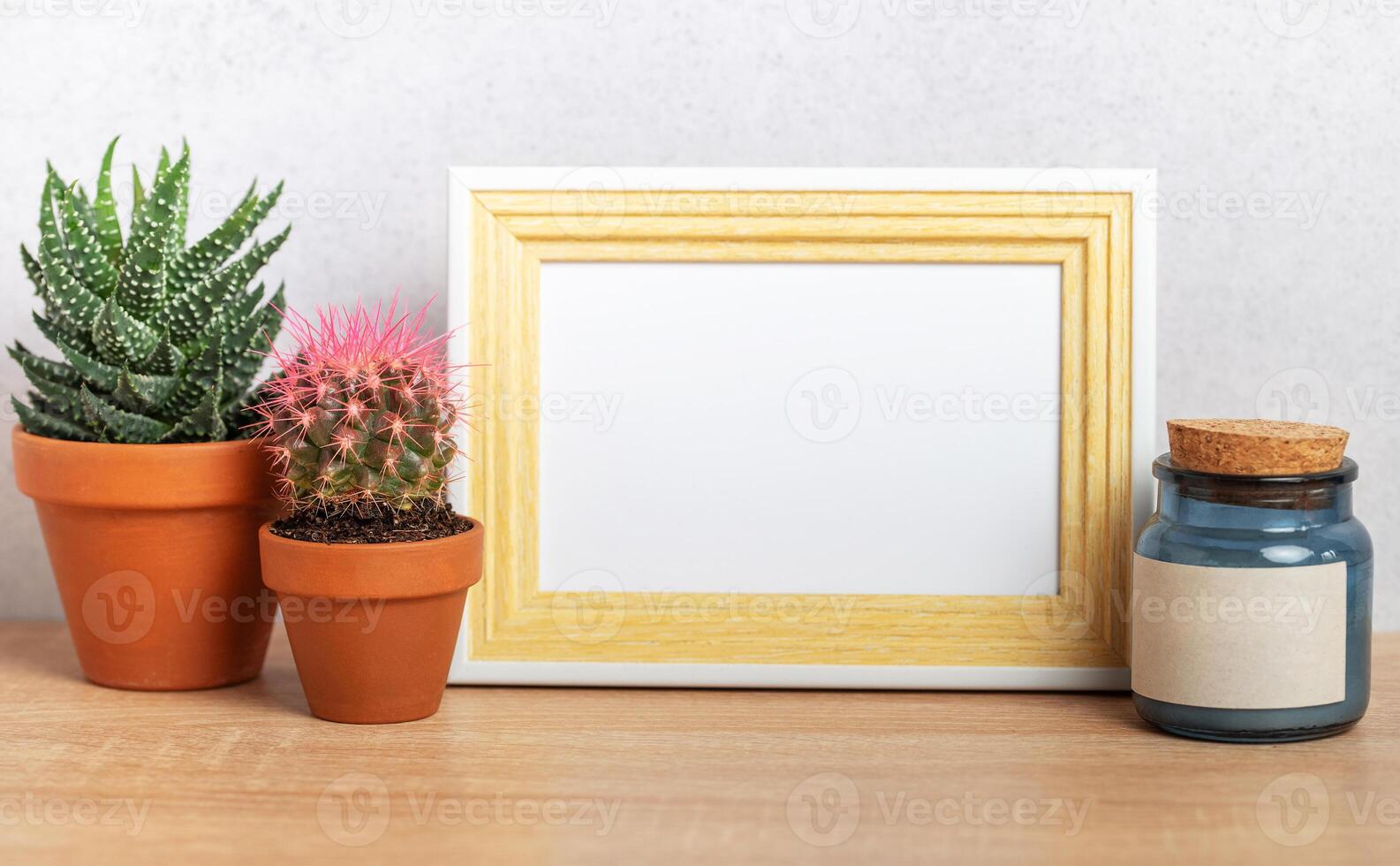 Empty frame mockup with cacti and blue jar on wooden table photo