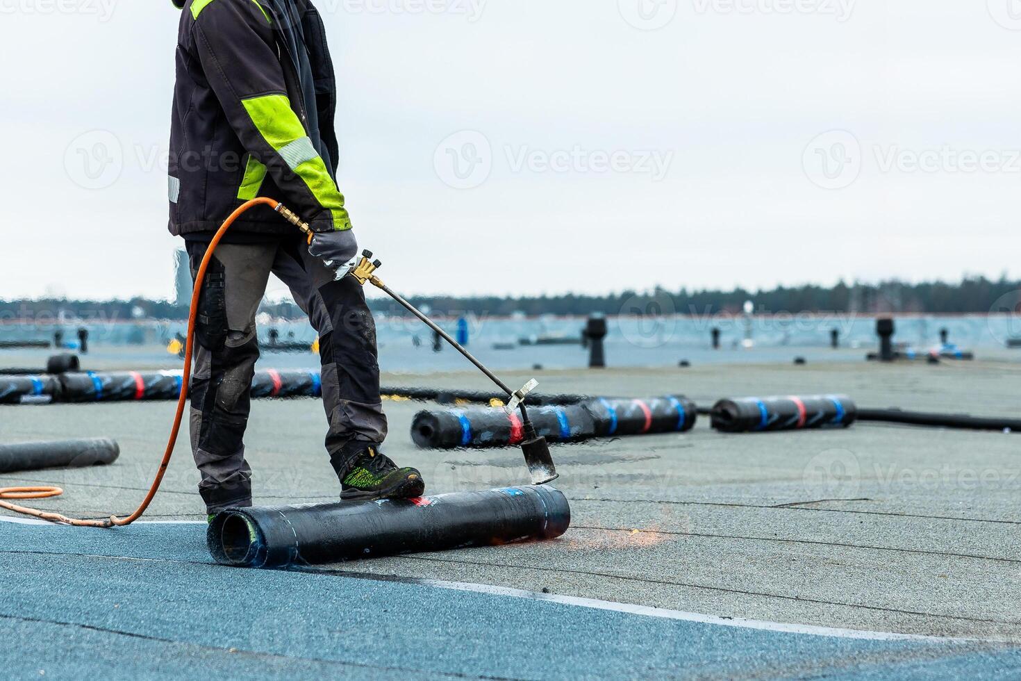 Worker Applies Torch On Roofing Material on Flat Rooftop Near Waterfront photo