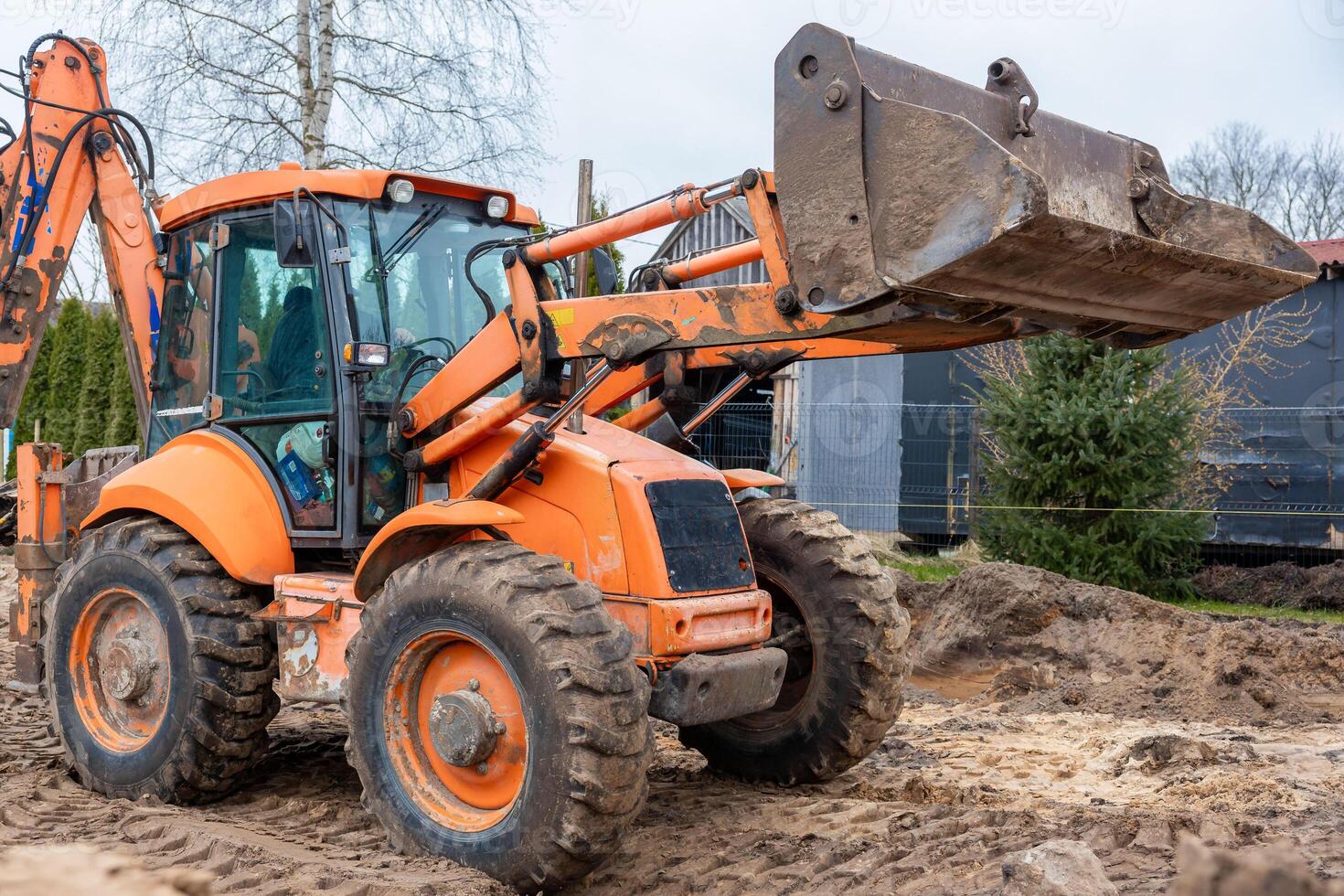 Orange Backhoe Loader on Construction Site with Raised Bucket photo